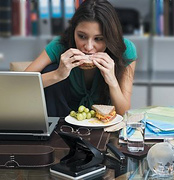 Woman eating at her work desk. - Copyright – Stock Photo / Register Mark