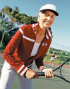 Older woman standing on tennis court with a racket ready. - Copyright – Stock Photo / Register Mark